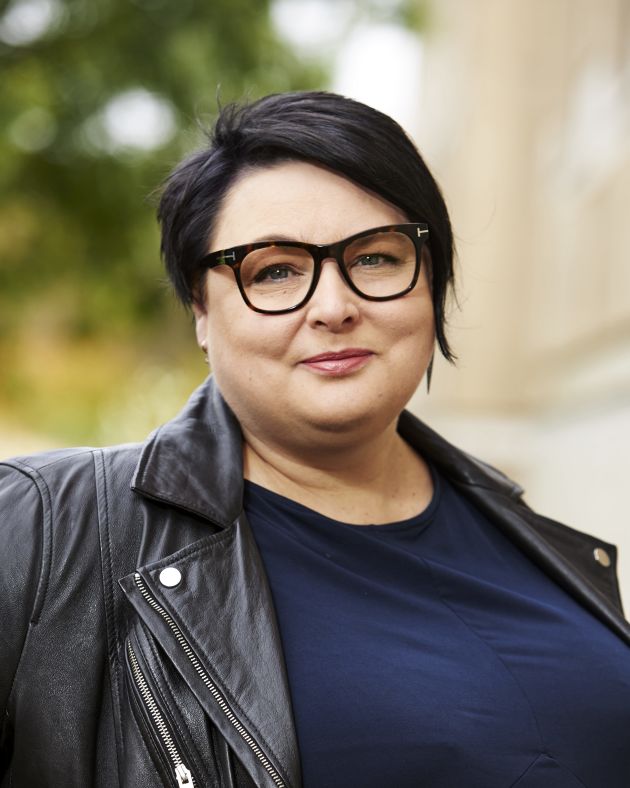 Photo of Lene Bull Christiansen. A white woman in a black t-shirt and black leather jacket, she has short black hair and is smiling