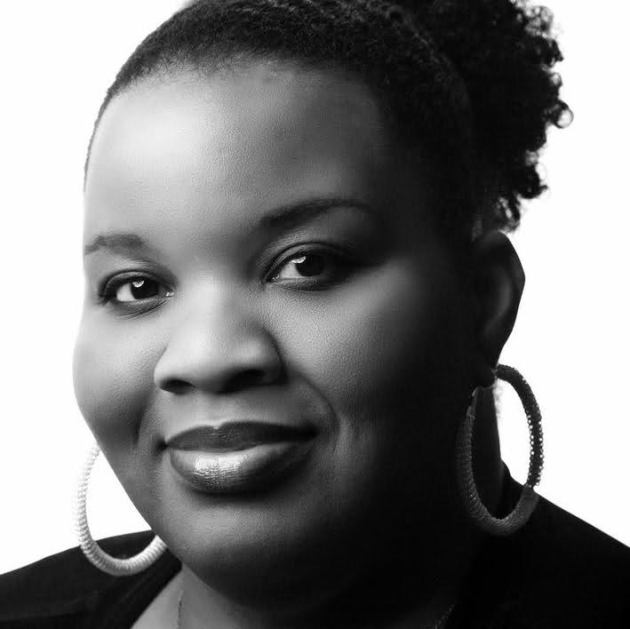 Headshot of Angel Austin. She is black woman, her hair is up off her face and she is smiling. She is wearing a black top and large hoop earrings.