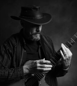 David wearing a hat strumming his guitar